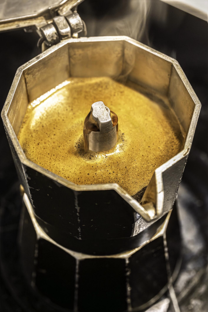 Close-up of freshly brewed Cuban coffee bubbling up in a moka pot on a stove, with steam rising from the open lid—a classic way to make Cuban coffee at home, just like you’d find in Miami.