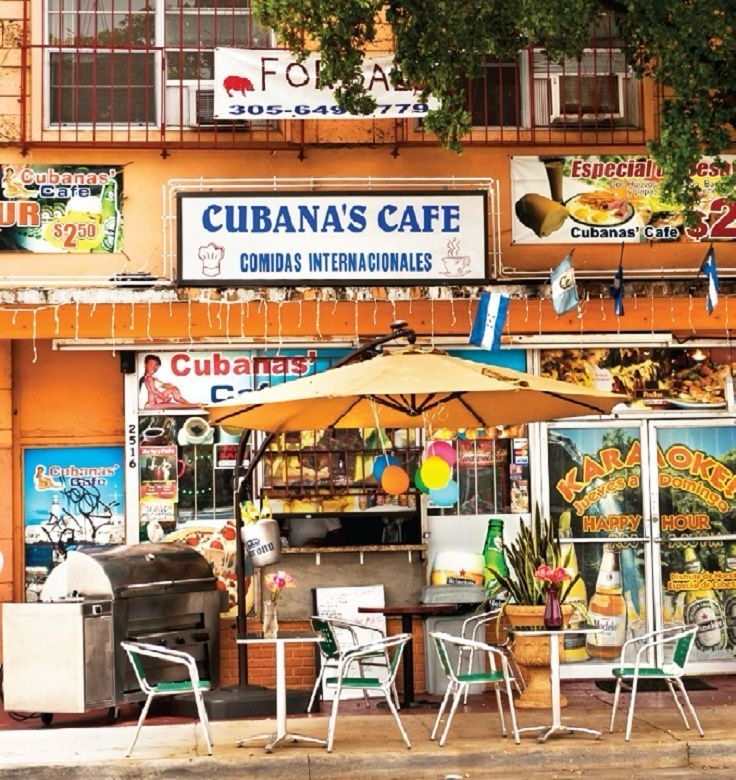 Image 4 Outdoor seating area in front of Cubana’s Cafe in Miami, featuring international food signs, a large umbrella, and metal chairs and tables on the sidewalk—perfect for sipping Cuban coffee or learning how to make it.
