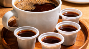 Image 5 A white mug of Cuban coffee on a wooden tray with four small containers of coffee, a metal pot, a pastry on a plate, and a palm leaf in the background—bringing the flavors of Miami right to your home.